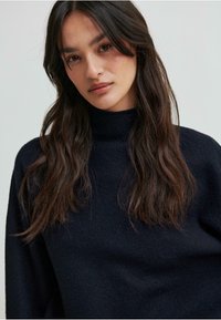 Ciemnoniebieski sweter typu golf z textured wykończeniem, posiadający długie rękawy i luźny krój. Prosty design bez zdobień.