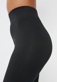 Leggings noires en tissu lisse et extensible avec une taille haute, présentant un design ajusté et une texture douce.