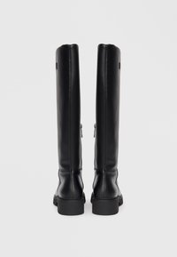 Bottes noires montantes en cuir lisse. Dotées d'un bout arrondi, d'un design minimaliste et de deux zips latéraux pour la fermeture.
