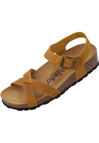Sandalia de cuero amarilla con correas entrelazadas, hebilla ajustable en el tobillo y suela de corcho texturizado. Diseño plano con suela de goma negra.