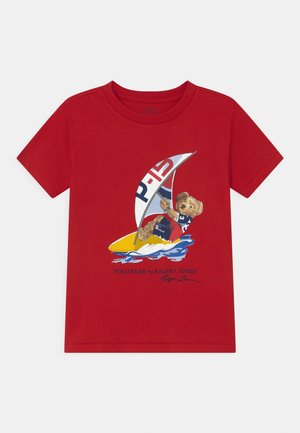 T-shirt enfant rouge à manches courtes avec un motif d'ours naviguant sur une planche de surf jaune avec une voile blanche, rouge et bleue.