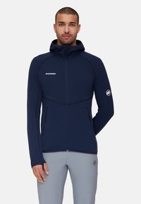 Giacca con cappuccio blu navy dal design aderente, con tasche con zip e cuciture in contrasto. Presenta il logo sul petto e sulla manica.