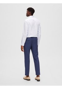 Hellblaues Langarmshirt, in karierte marineblaue Hose gesteckt. Glatte Textur, mit einem Knopfdetail an den Gesäßtaschen. Schuhe in neutralen Farben.