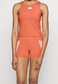 Completo sportivo Nike composto da un top arancione senza maniche con logo, abbinato a pantaloni arancioni con pannelli laterali in un rosa chiaro a contrasto.