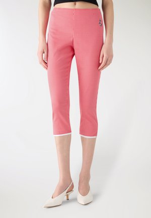 Donne che indossano pantaloni corti a quadretti rossi e bianchi e tacchi bianchi con cinturino, in piedi contro uno sfondo chiaro e uniforme.