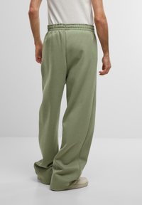 Pantalons de survêtement verts, amples, avec une taille élastique, fabriqués en tissu doux, présentant une texture lisse et une coupe large.