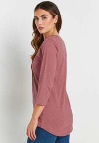 Top lungo a maniche con orlo arrotondato in color rosa, dalla vestibilità comoda, realizzato in un tessuto morbido con una leggera trama. Presenta un colletto a V.