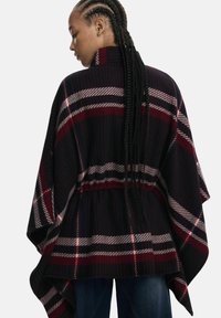 Schwarz-rot-weiß karierter Poncho mit hohem Kragen, lockerer Passform und dekorativem Kordelzug in der Taille für anpassbare Form und Stil.