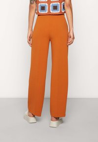 Breda byxor i en rik orange färg med en slät textur, med hög midja och avslappnad passform, i kombination med lätta platåskor.
