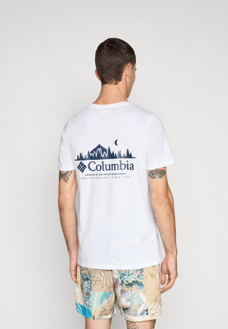 Weißes Baumwoll-T-Shirt mit einem navyfarbenen Grafikdesign von Bergen und Bäumen auf dem Rücken, ergänzt durch den Schriftzug "Columbia" und ein maritimes Muster auf den Shorts.