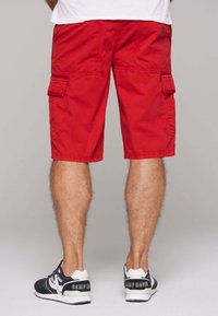 Rode cargoshorts van katoen, met zijzakken en een losse pasvorm. Gecombineerd met marineblauwe en witte sportschoenen.
