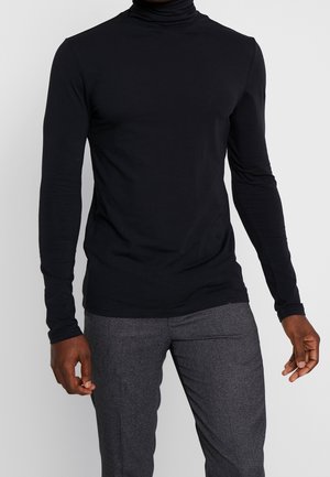 Chandail à col roulé noir à manches longues, en tissu doux et extensible. Design ajusté avec un col haut, associé à un pantalon gris sur mesure.