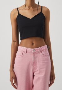 Top cropped nero con scollatura a onde; abbinato a jeans a vita alta rosa chiaro. Tessuto morbido; vestibilità casual.