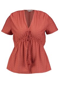 Lyhytheimá, korallinvärinen toppi, jossa on syvä V-pääntie ja tekstuurinen timanttikuvio; kerätty vyötärö, jossa on naru ja tupsuyksityiskohta.