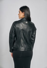 Černá kožená bunda s přiléhavým střihem a švovými detaily, s visačkou na zádech. Nositelná s černou sukní. Hladká textura.