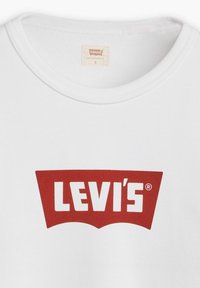 T-shirt bianco in cotone con un grande logo rosso Levi's® in design curvo, posizionato centralmente sul petto. Maniche corte e scollatura rotonda.