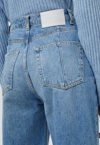 Jeans de mezclilla de tiro alto en azul claro con bolsillos traseros y costuras en contraste. Presentan una etiqueta de cuero blanca en la cinturilla.