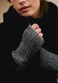 Szare rękawiczki z prążkowanego, miękkiego materiału, noszone przez osobę w czarnym płaszczu. Zbliżenie na dłonie i szczegóły stroju.