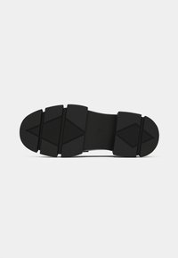 Black rubber shoe sole with textured grip pattern, featuring segmented sections and a smooth central area, designed for traction and durability.