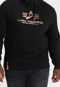 Felpa con cappuccio nera in misto cotone, con tasca a marsupio frontale, logo metallico, cappuccio con coulisse e polsini e orlo a coste.