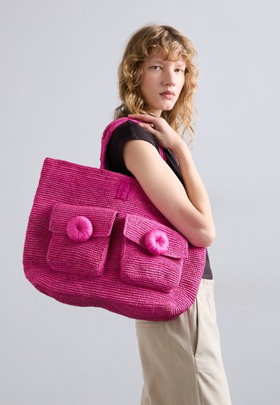 Bolsa tote tejida de color rosa brillante con dos bolsillos frontales, cada uno con un cierre de botón redondo. La tela texturizada realza el interés visual.