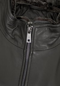 Nahaufnahme einer schwarzen Lederjacke mit silbernem Reißverschluss und weichem, dunklem Pelzbesatz am Kragen.