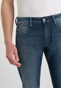 Jeans en denim de couleur bleu foncé avec un léger délavage, design à cinq poches, fermeture par bouton en métal et passants de ceinture visibles à la taille.