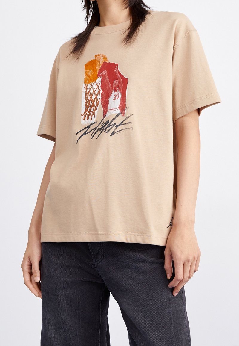 T-shirt en coton beige avec un imprimé graphique d'un joueur de basket et d'un panier dans des tons rouges et orange. Manches courtes, coupe décontractée.