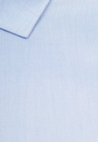 Lichtblauwe stof met smalle witte strepen, met een gladde textuur en een gevouwen hoek. Materiaal lijkt geweven katoen te zijn.