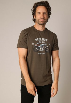T-shirt marron en coton, avec un motif de moto vintage et le texte "Deeluxe Road Club" ainsi qu'un col rond. Design simple et ajusté.
