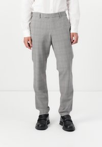 Pantaloni da uomo a quadri grigi con una vestibilità sartoriale, gamba piatta e passanti per la cintura, abbinati a scarpe nere slip-on. Il tessuto presenta un sottile motivo a quadretti.