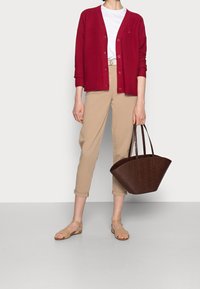 Röd cardigan, vit t-shirt, beige byxor och brun texturerad toteväska. Sandalerna är ljusbeiga med ett remdesign.
