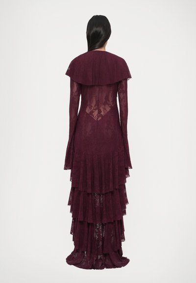 Abito lungo color borgogna in pizzo con balze a strati e scollatura smerlata, caratterizzato da schiena trasparente e silhouette aderente.