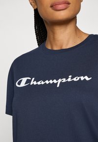 Tamno plava pamučna majica kratkih rukava s okruglim izrezom, s bijelim tekstom "Champion" na prsima.