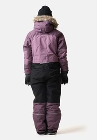 Isolierter Winteroverall in Lila und Schwarz, mit Kapuze und Kunstfellbesatz, elastischen Bündchen und reflektierenden Details an den Ärmeln.