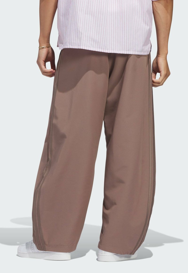 Person wearing loose brown pants and white sneakers, shown from the back with a striped shirt partially visible.