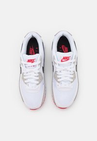 Vita Nike-sneakers med meshoch lädermaterial, rund tådesign, svarta accenter och en röd Nike-logotyp på tungan och sulan.