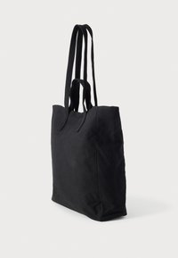 Μαύρη υφασμάτινη τσάντα ώμου με δύο μακριές, διπλές λαβές· ορθογώνιο σχήμα· υφή με ανάγλυφη επιφάνεια· μινιμαλιστικός σχεδιασμός· χωρίς ορατά μεταλλικά μέρη ή διακοσμητικά.