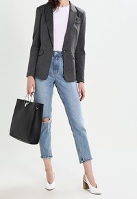 Blazer grigio su misura sopra una maglietta bianca, abbinato a jeans azzurri chiari con strappi, borsa a tracolla nera e scarpe con tacco bianche.