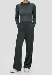 Top lungo fitted grigio scuro con collo alto, abbinato a pantaloni larghi a vita alta e scarpe da ginnastica chiare.