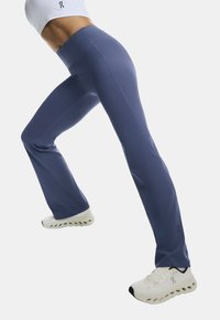 Granatowe, rozszerzane spodnie sportowe z wysokim stanem, wykonane z elastycznego materiału, w połączeniu z białymi butami sportowymi z teksturowaną podeszwą.