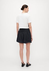 Hvit croppet t-skjorte og svarte shorts med elastisk midje. Bomullstopp med korte ermer; nylonshorts med voluminøst design og glatt tekstur.