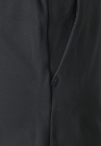 Tissu noir avec une petite étiquette en caoutchouc noir embossée du mot « ONLY » près d'une couture ou d'un pli.