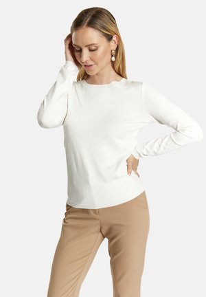 Witte langekorte top met een ronde halslijn, zachte textuur en een aansluitend ontwerp, gecombineerd met tan broek. Geen patronen of extra accenten.