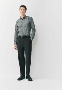 Herren Langarmhemd mit dunklem Muster, kombiniert mit dunklen Hosen und schwarzen Lederschuhen. Das Hemd hat einen Kragen und eine Knopfleiste.