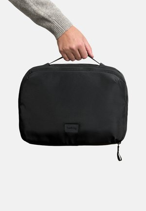 Borsa nera con cerniera, dalla forma rettangolare sottile, realizzata in tessuto e dotata di manico superiore. Presenta una toppa con logo e un design elegante.