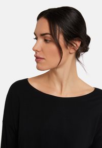 Svart långärmad topp med bred båtformad halsringning och lös passform. Slät textur, minimalistisk design, inga synliga mönster eller hårdvara.