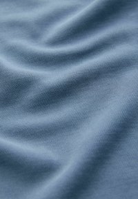Heledsinine kangas sujuva tekstuuriga, millel on peened kortsud ja ühtlane kudumise muster.