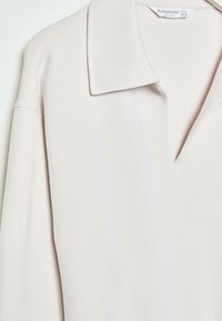 Hellrosa Langarm-Polohemd mit weicher Textur, das einen spitzen Kragen und ein dezentes V-Ausschnitt-Design bietet.