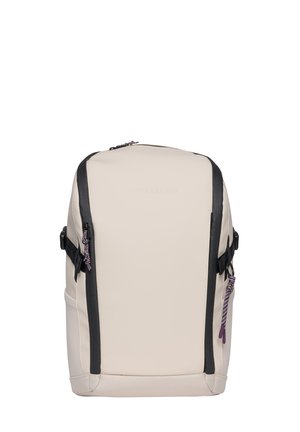 Beige rektangulær ryggsekk med svarte vertikale glidelåser, sidelommer i mesh, justerbare stropper og lilla glidelåstrekk.
